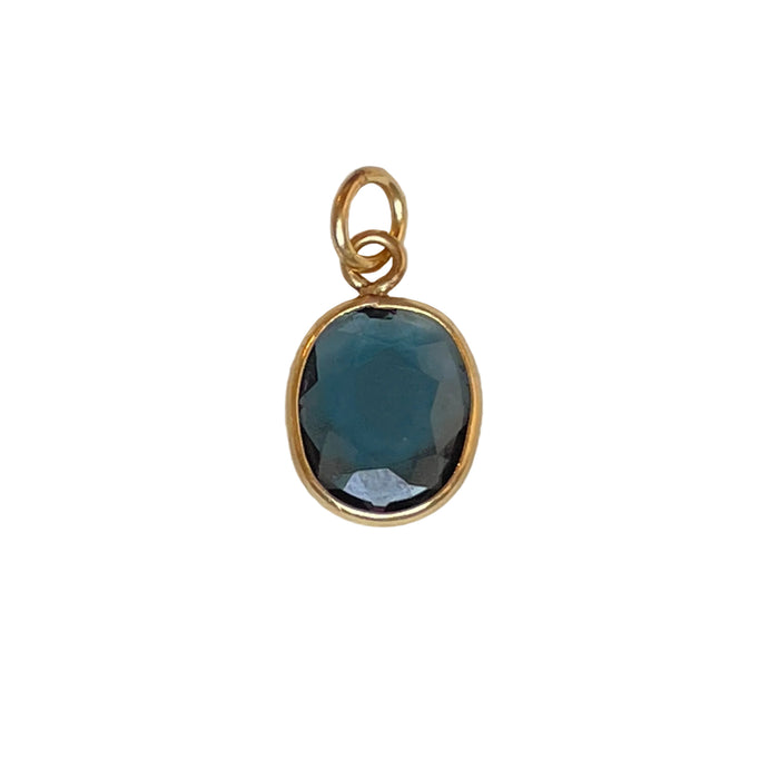 Gold charm with a blue tourmaline on a white background
