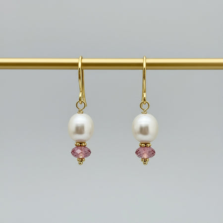 Pair of pearl earrings with gold and pink beads on a gray background