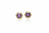 Hexagonal gold earrings with purple gemstones on a light blue background