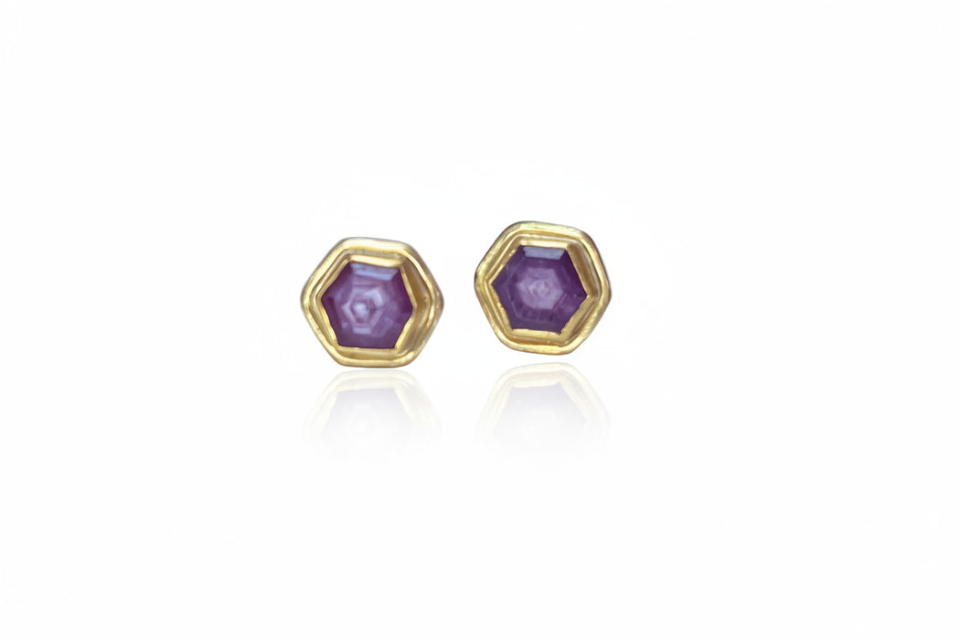 Hexagonal gold earrings with purple gemstones on a light blue background
