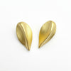 Two gold seed-shaped earrings on a gray surface