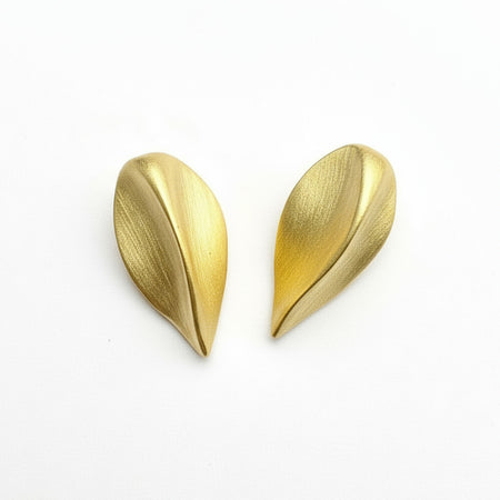 Two gold seed-shaped earrings on a gray surface