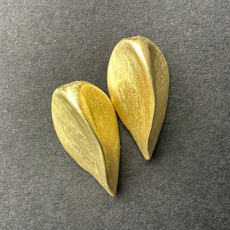 Two gold seed-shaped earrings on a dark gray background