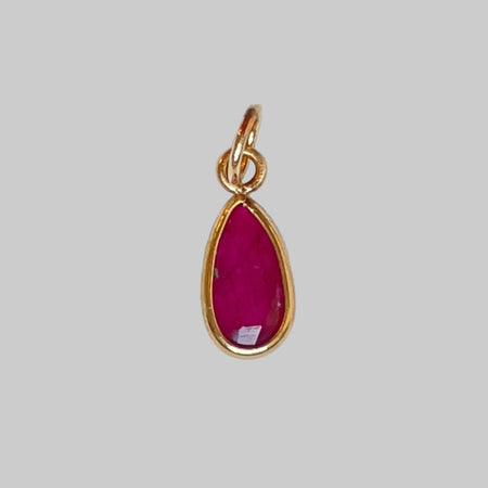 Gold charm with a ruby on a light gray background