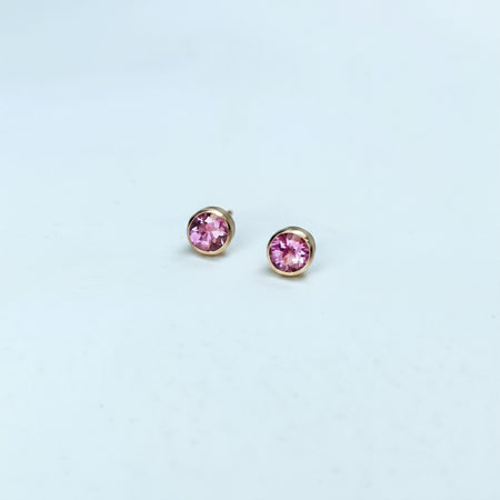 Pair of pink sapphire stud earrings on a light blue background