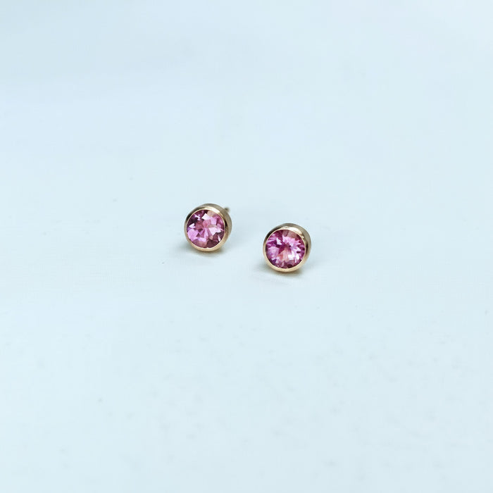Pair of pink sapphire stud earrings on a light blue background