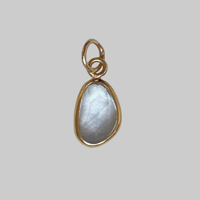 Gold charm with a teardrop-shaped aquamarine on a light gray background