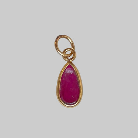Gold charm with a ruby on a light grey background