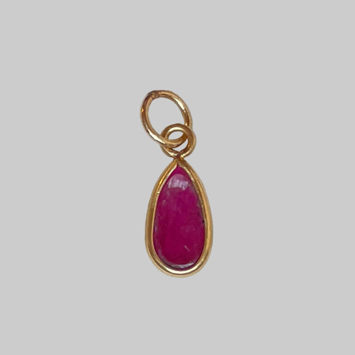 Gold charm with a ruby on a light grey background